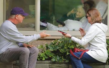 A couple visit with elderly through window and phone to practice social distancing